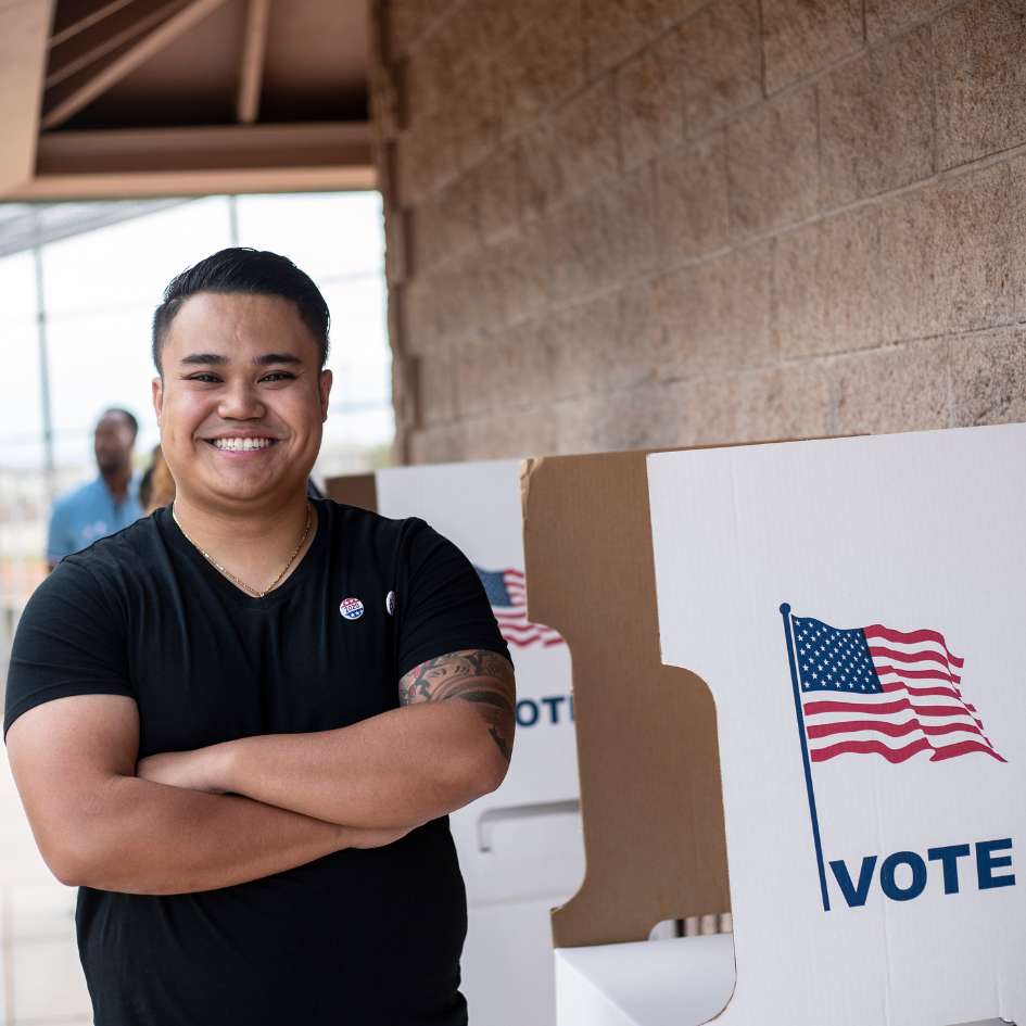 Man standing beside voting booth smiling at camera