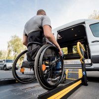 A man in a wheelchair moves to the lift of a specialized vehicle.