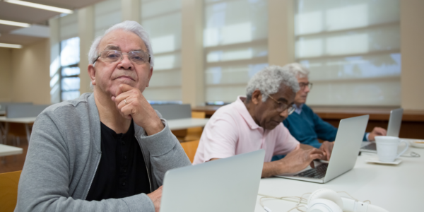 Photo of older adults working on laptops. One is looking at the camera
