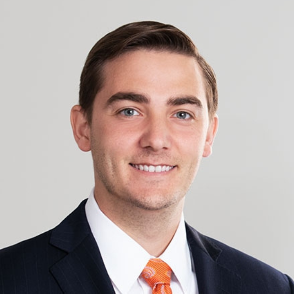 Photo of Tim Scott a young White man with short dark hair wearing a black suit, white collared shirt and orange tie.