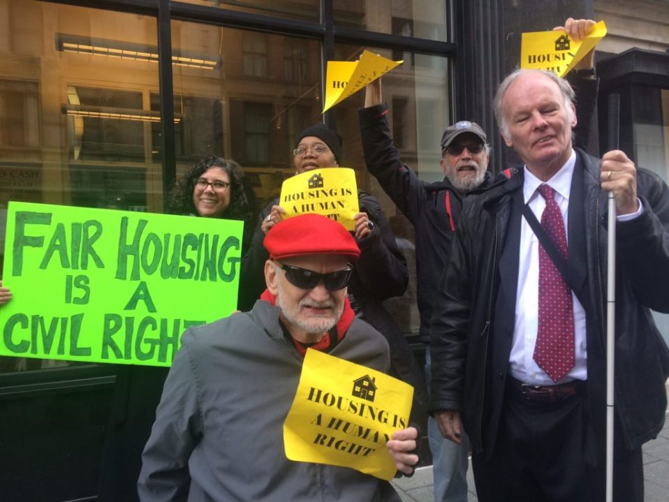Disability Rights Activists holding yellow signs that say Housing is a "Human Right" and a green sign that says, "Fair Housing is a Civil Right."
