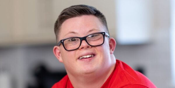 Young man with short brown hair smiling at camera wearing black glasses and a red tshirt