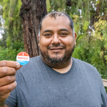 Man smiling and holing an 'I voted' Sticker