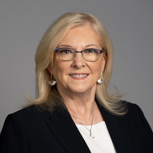 Robin Murphy is a White woman with shoulder length blond hair. She smiles and wears black rimmed glasses, dangle earrings, and a white blouse under a black blazer.