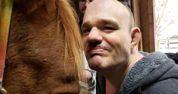 Troy is an older White man smiling next to a horse.