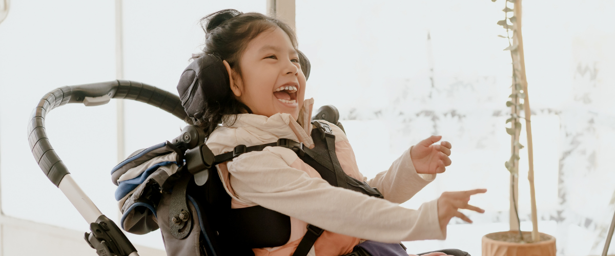 Young girl in wheelchair with seatbelt harness smiling big