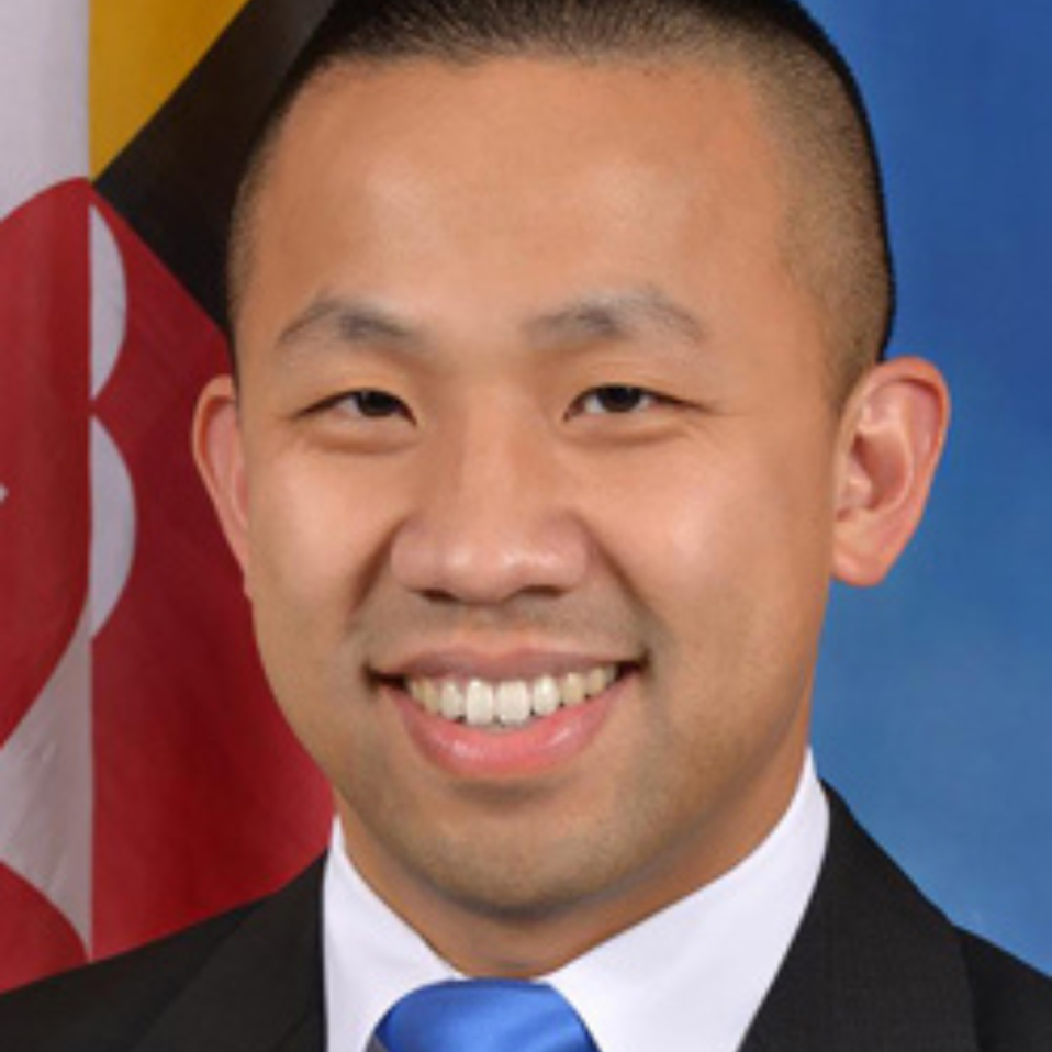 Photo of Clarence Lam an Asian man with short Black hair wearing black suit, white collared shirt and blue tie.