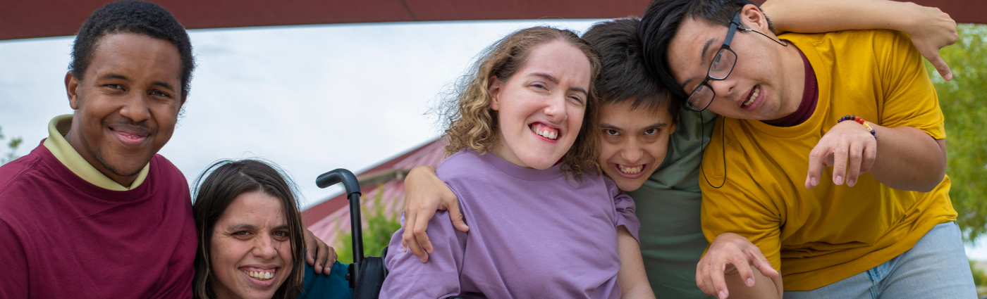 A diverse group of young adults hugging and smiling at the camera