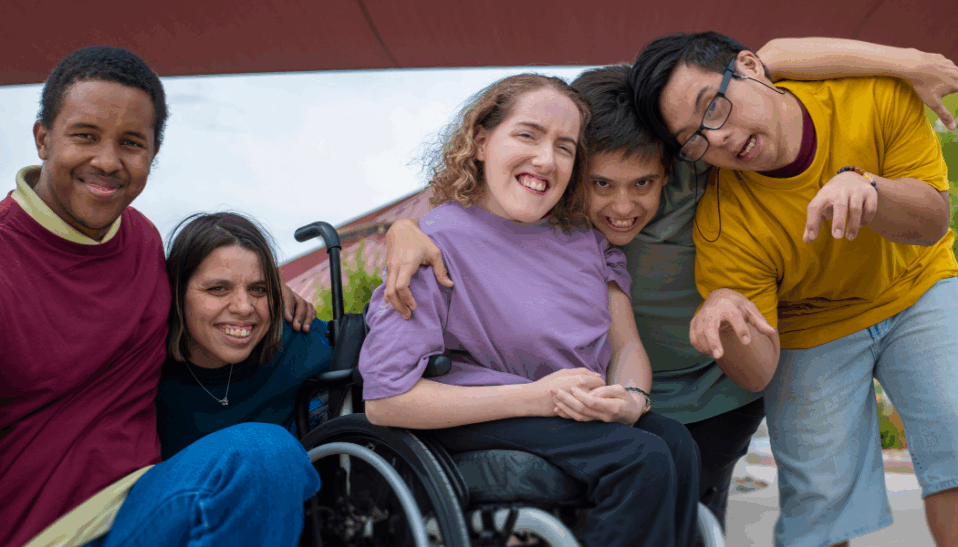 A diverse group of young adults hugging and smiling at the camera