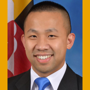 Photo of Clarence Lam an Asian man with short Black hair wearing black suit, white collared shirt and blue tie.