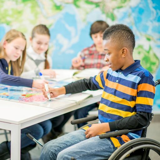 Boy in wheelchair sitting at table with other kids. All are l